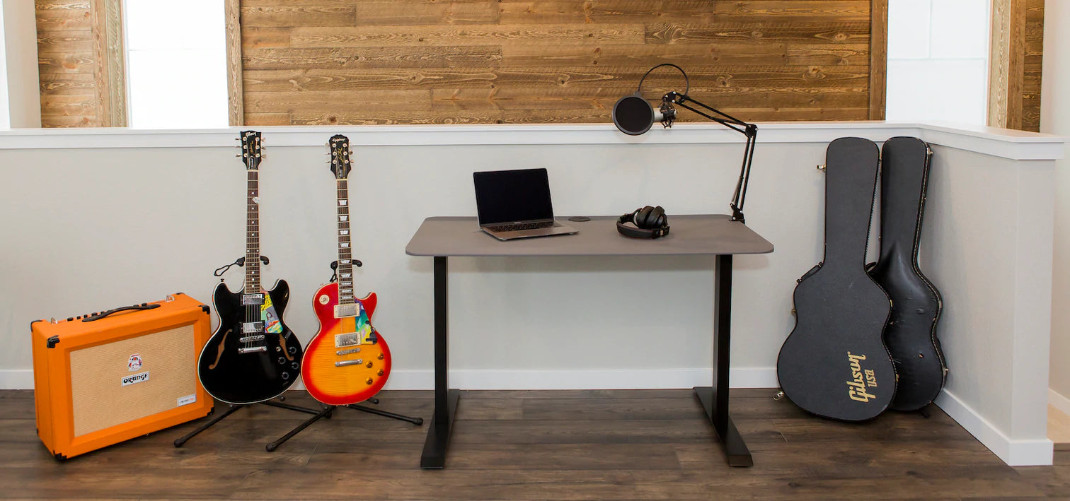 sit and stand adjustable desk shown with guitars and orange amp on left and right